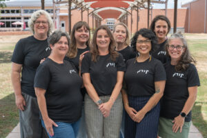 Eight people stand and smile in a breezeway in matching black shirts displaying a pro-tactile "TDBP."