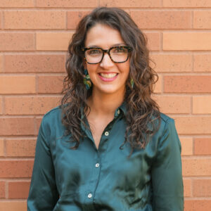Kaycee smiles in front of a brick wall.